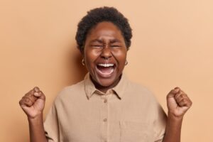 Mad emotional dark skinned woman goes out of control expresses rage and fury clenches fists screams